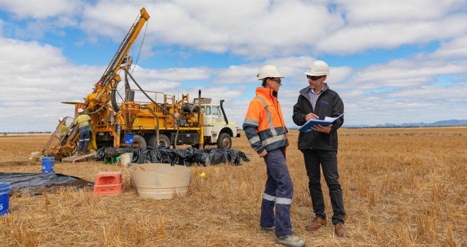 Two people standing in front of a drill in a field