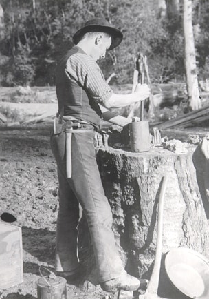 An old black and white photo of a miner crushing quartz in a pot.